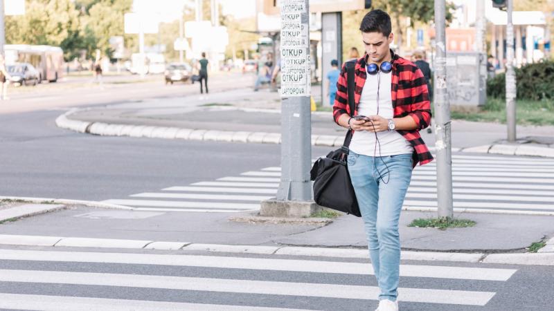 young man with smartphone crossing street