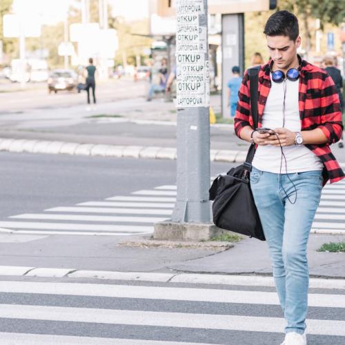 young man with smartphone crossing street